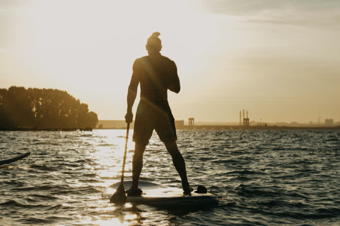 A paddleboarder standing on calm water at golden hour