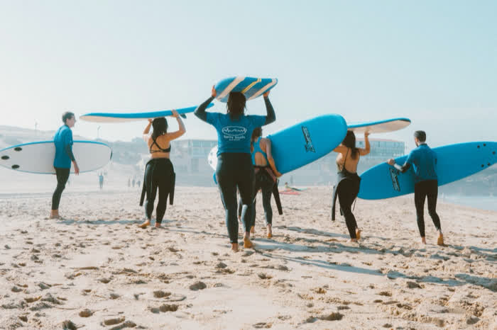 A group carrying surfboards down to the water